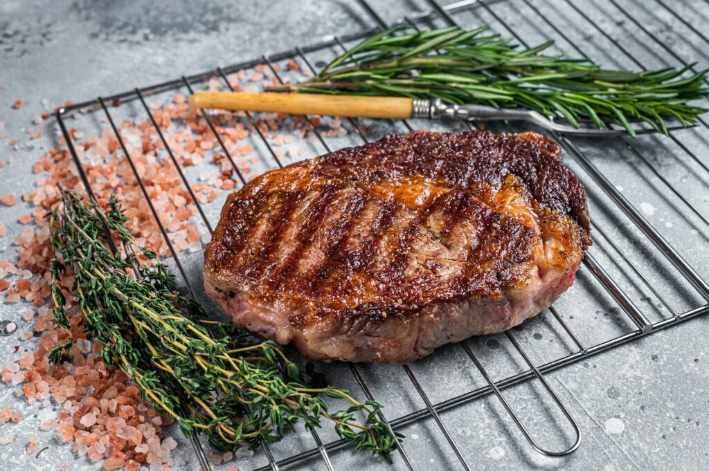 BBQ grilled rib-eye steak, rib eye beef meat on a grill with herbs. Gray background. top view